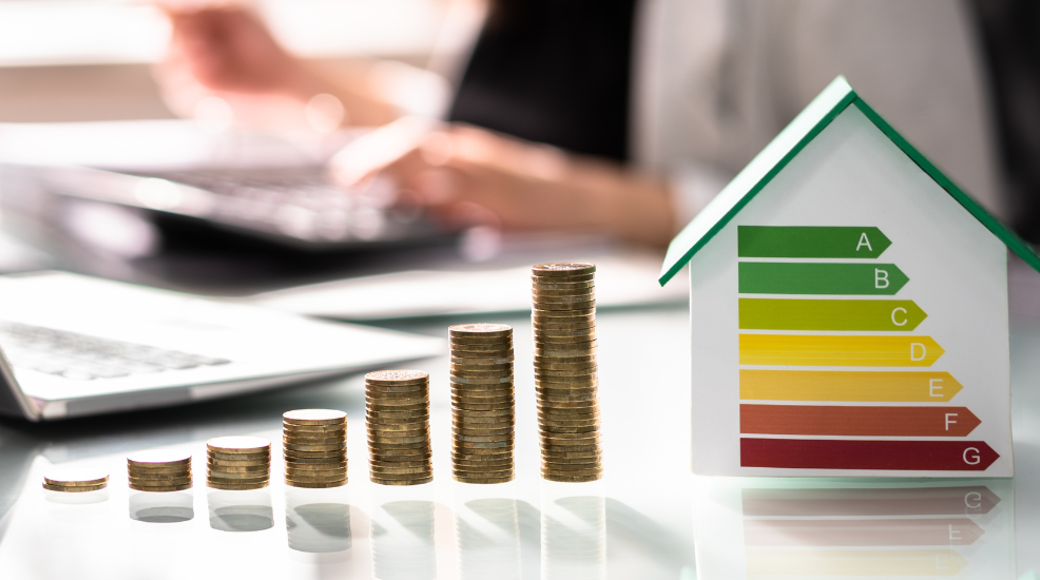 Stacked Coins In A Row Increasing In Height Each Time Next to A Small Toy House
