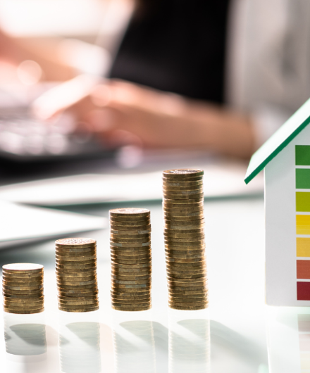 Stacked Coins In A Row Increasing In Height Each Time Next to A Small Toy House