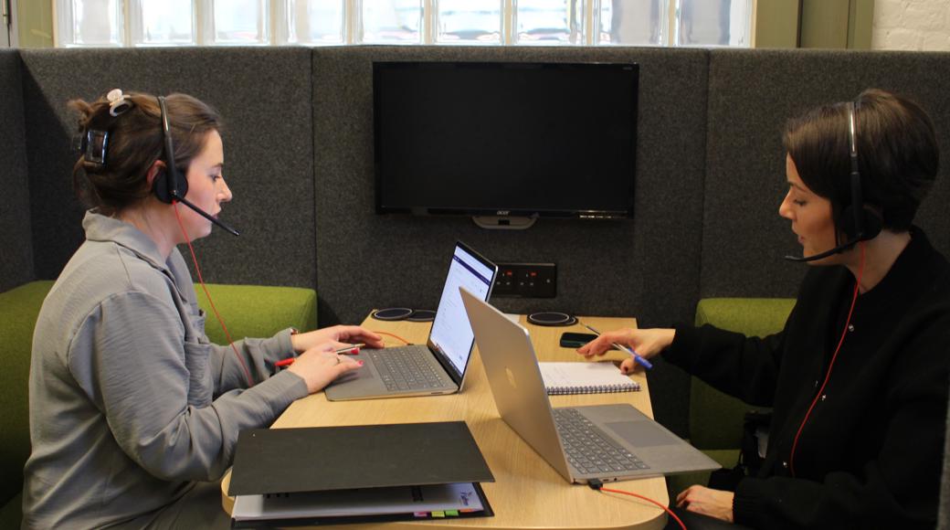 Two Members Of Saffron Sat At A Desk